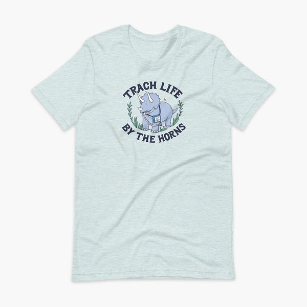 A happy triceratops dinosaur that has a trach or tracheostomy and a vent or ventillator to help him breathe. He also has a g-tube or gastronomy tube. There is text wrapping around the dinosaur that says Trach Life By The Horns. It is on a heather prism ice blue adult t-shirt.