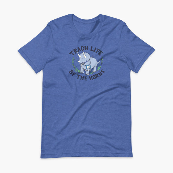 A happy triceratops dinosaur that has a trach or tracheostomy and a vent or ventillator to help him breathe. He also has a g-tube or gastronomy tube. There is text wrapping around the dinosaur that says Trach Life By The Horns. It is on a heather true royal adult t-shirt.