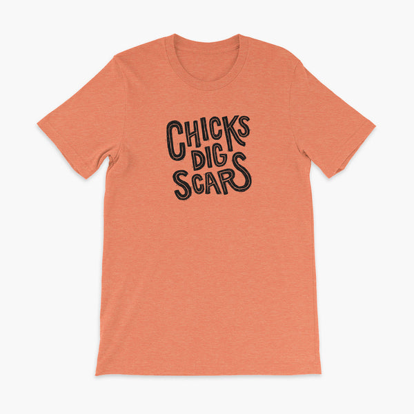 Black textured and distressed hand lettered typography that says chicks dig scars on a heather orange t-shirt
