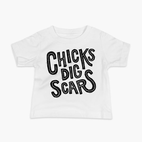 Black textured and distressed hand lettered typography that says chicks dig scars on a white t-shirt