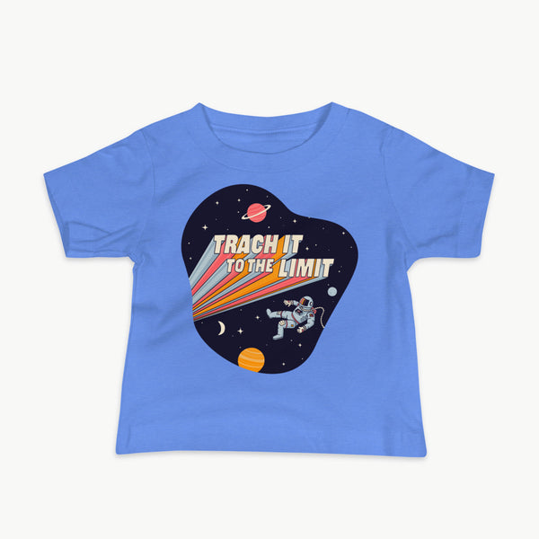 An illustration of an astronaut with a trach and tubing floating in outer space surrounded by stars and planets. Behind the astronaut, bold retro text reads “Trach It to the Limit,” with colorful light trails shooting from the words like a rocket launch. The design appears on a dark background. It is on a infant Columbia blue t-shirt.