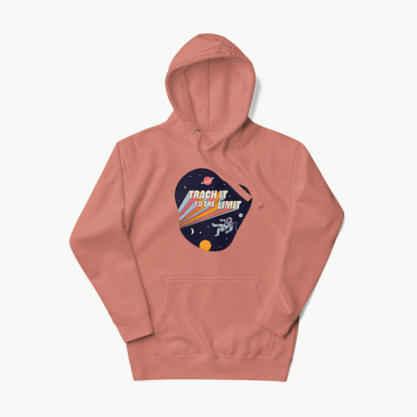 An illustration of an astronaut with a trach and tubing floating in outer space surrounded by stars and planets. Behind the astronaut, bold retro text reads “Trach It to the Limit,” with colorful light trails shooting from the words like a rocket launch. The design appears on a dark background. It is on a dusty rose adult hoodie.