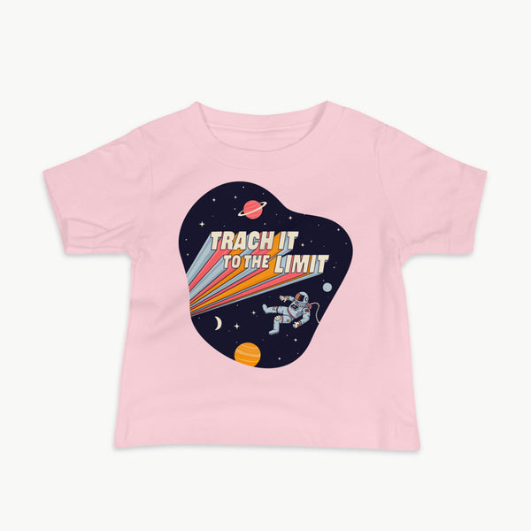 An illustration of an astronaut with a trach and tubing floating in outer space surrounded by stars and planets. Behind the astronaut, bold retro text reads “Trach It to the Limit,” with colorful light trails shooting from the words like a rocket launch. The design appears on a dark background. It is on a infant pink t-shirt.