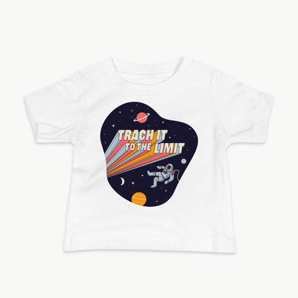 An illustration of an astronaut with a trach and tubing floating in outer space surrounded by stars and planets. Behind the astronaut, bold retro text reads “Trach It to the Limit,” with colorful light trails shooting from the words like a rocket launch. The design appears on a dark background. It is on a infant white t-shirt.