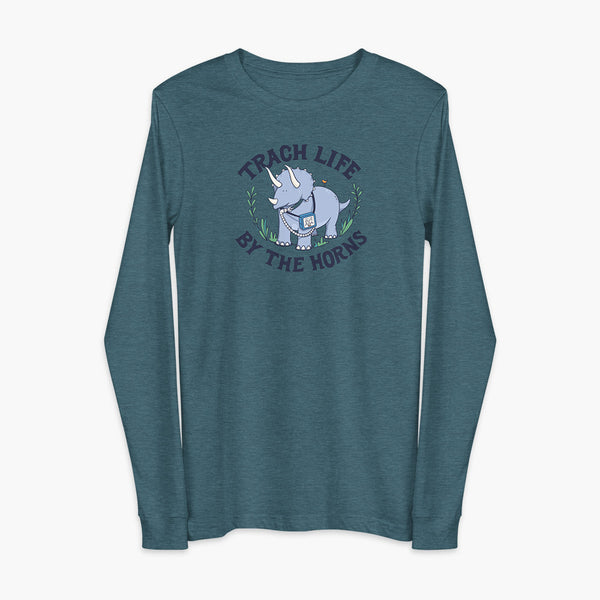A happy triceratops dinosaur that has a trach or tracheostomy and a vent or ventillator to help him breathe. He also has a g-tube or gastronomy tube. There is text wrapping around the dinosaur that says Trach Life By The Horns. It is on a heather deep teal adult long sleeve t-shirt.