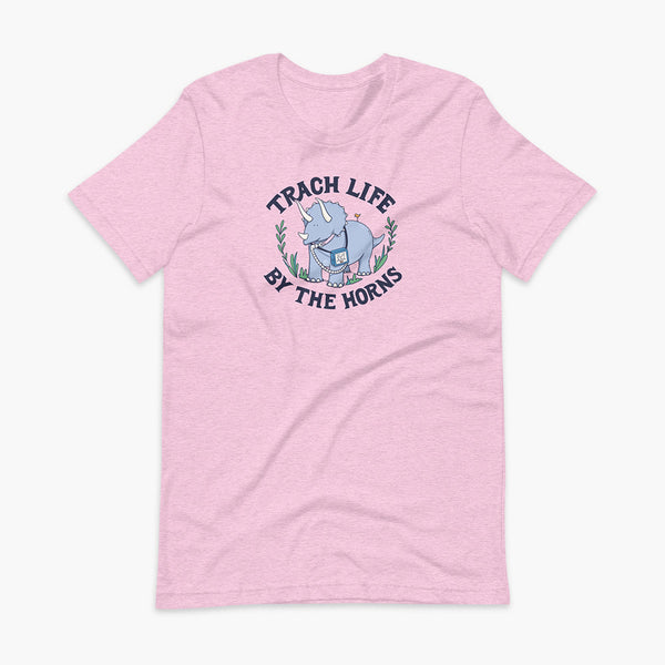 A happy triceratops dinosaur that has a trach or tracheostomy and a vent or ventillator to help him breathe. He also has a g-tube or gastronomy tube. There is text wrapping around the dinosaur that says Trach Life By The Horns. It is on a heather prism lilac adult t-shirt.