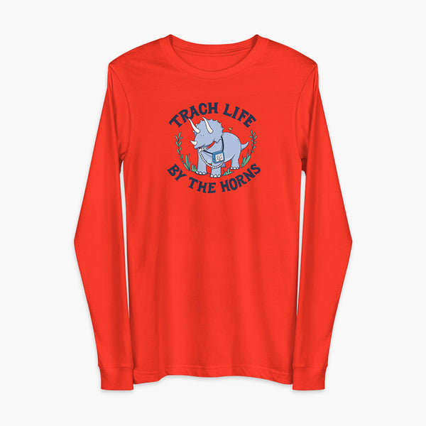 A happy triceratops dinosaur that has a trach or tracheostomy and a vent or ventillator to help him breathe. He also has a g-tube or gastronomy tube. There is text wrapping around the dinosaur that says Trach Life By The Horns. It is on a poppy adult long sleeve t-shirt.
