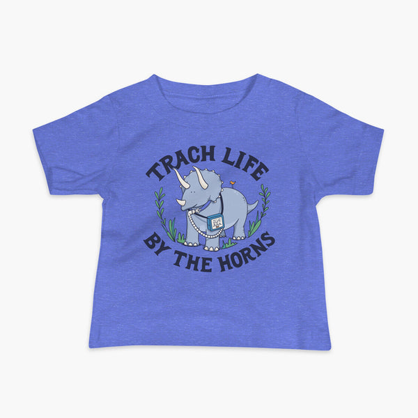 A happy triceratops dinosaur that has a trach or tracheostomy and a vent or ventillator to help him breathe. He also has a g-tube or gastronomy tube. There is text wrapping around the dinosaur that says Trach Life By The Horns. It is on a heather blue infant t-shirt.