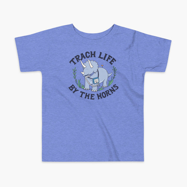 A happy triceratops dinosaur that has a trach or tracheostomy and a vent or ventillator to help him breathe. He also has a g-tube or gastronomy tube. There is text wrapping around the dinosaur that says Trach Life By The Horns. It is on a heather blue kids  t-shirt.
