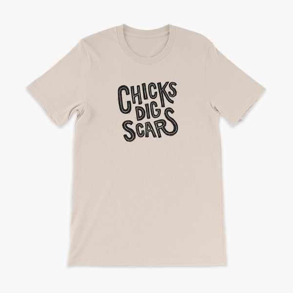 Black textured and distressed hand lettered typography that says chicks dig scars on a soft creme t-shirt