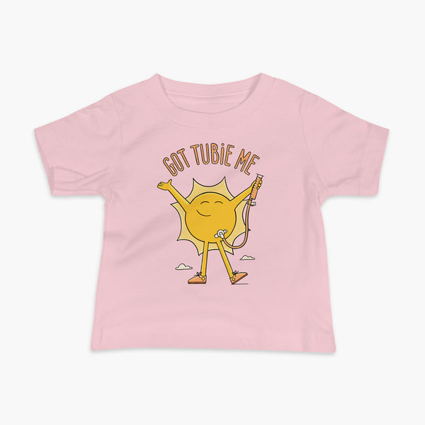 A happy sun stands confidently in tennis shoes holding a g-tube or a gastronomy tube with a stoma for StomaStoma with the text Got Tubie Me above him on a infant pink t-shirt 