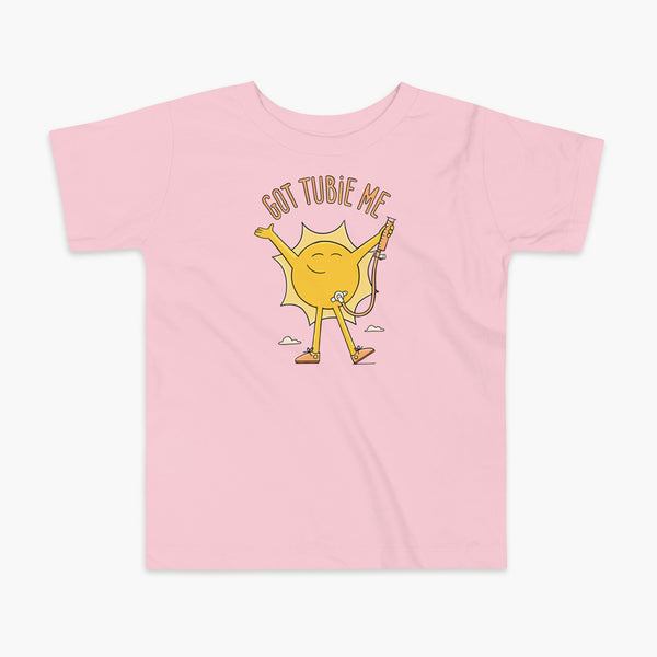 A happy sun stands confidently in tennis shoes holding a g-tube or a gastronomy tube with a stoma for StomaStoma with the text Got Tubie Me above him on a kids pink t-shirt 