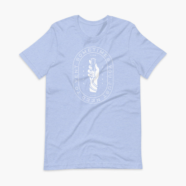 Text that says Sometimes You Just Need To Vent wrapping around a hand holding a syringe or venting tube that is connected to a g-tube or gastronomy tube and mic-key button. There is additional text that says StomaStoma and Tube Life. On a heather blue adult t-shirt.