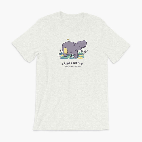 A Hippo or Hippopotamus with an ostomy bag — also known as a Hippopostomy. He is standing in some foliage smiling and has a bird on his back on an ash adult t-shirt.
