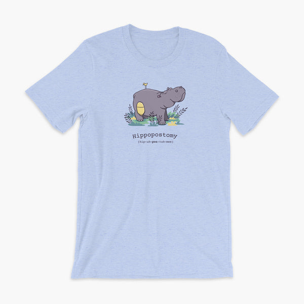 A Hippo or Hippopotamus with an ostomy bag — also known as a Hippopostomy. He is standing in some foliage smiling and has a bird on his back on a heather blue adult t-shirt.