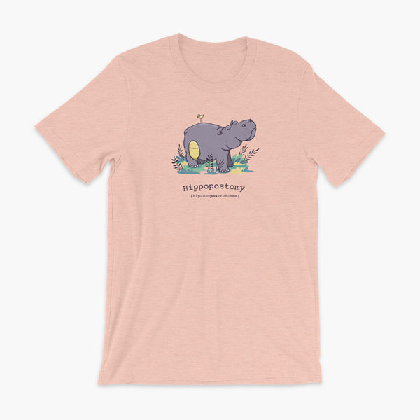 A Hippo or Hippopotamus with an ostomy bag — also known as a Hippopostomy. He is standing in some foliage smiling and has a bird on his back on a heather prism peach adult t-shirt.
