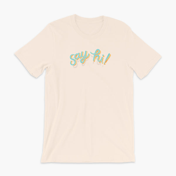 Floating say hi! script text on a soft creme adult t-shirt