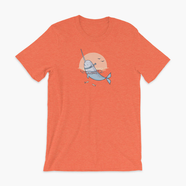 A Narwhal that has a trach or tracheostomy pokes his head and horn through the water in front of a setting sun. He has a naturally built in stoma. It is on a heather orange adult t-shirt.