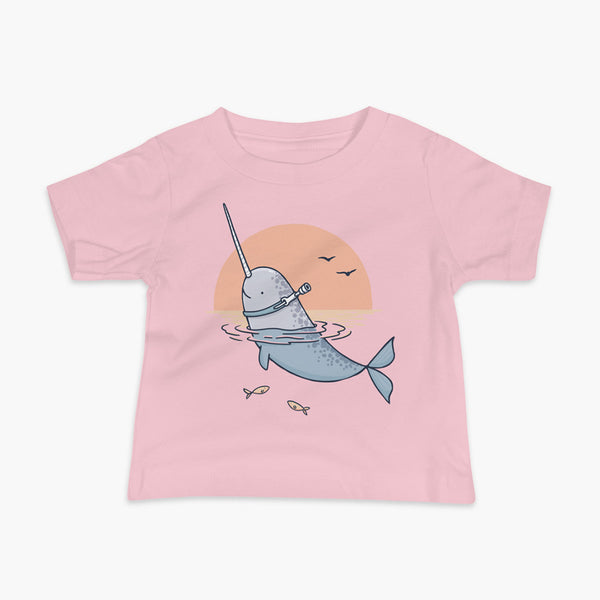 A Narwhal that has a trach or tracheostomy pokes his head and horn through the water in front of a setting sun. He has a naturally built in stoma. It is on a pink infant t-shirt.