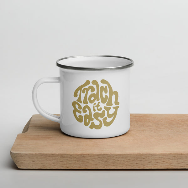 A white enamel mug with a white coating and silver rim with the text "Trach it Easy" in gold hand lettering on the side.