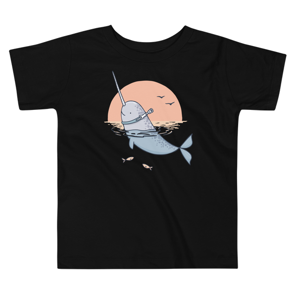 A Narwhal that has a trach or tracheostomy pokes his head and horn through the water in front of a setting sun. He has a naturally built in stoma. It is on a black kids t-shirt.