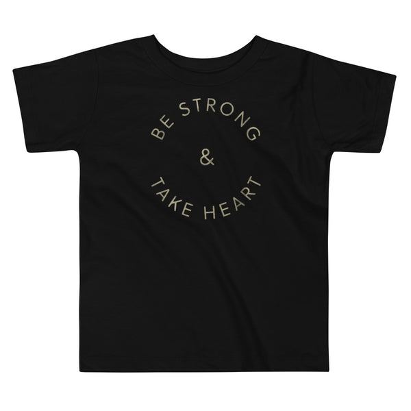 Gold text that says Be Strong & Take Heart in a circle on a kids black t-shirt by StomaStoma for g-tube and trach life empowerment.
