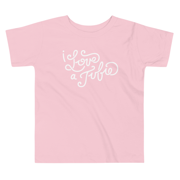 White Hand-drawn script or lettering that says I love a tubie on a  pink kids t-shirt for the g-tube or stoma.