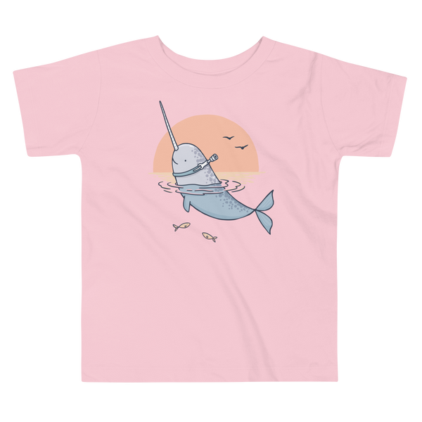 A Narwhale that has a trach or tracheostomy pokes his head and horn through the water in front of a setting sun. He has a naturally built in stoma. It is on a pink kids t-shirt.