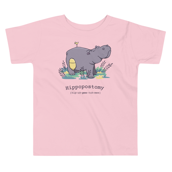 A Hippo or Hippopotamus has a stoma with an ostomy bag — also known as a Hippopostomy. He is standing in some foliage smiling and has a bird on his back on a pink kids t-shirt.