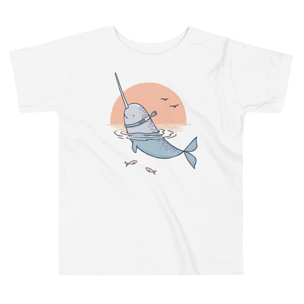 A Narwhal that has a trach or tracheostomy pokes his head and horn through the water in front of a setting sun. He has a naturally built in stoma. It is on a white kids t-shirt.
